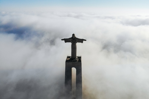 雲上にそびえ立つ塔上で手を広げた神の像